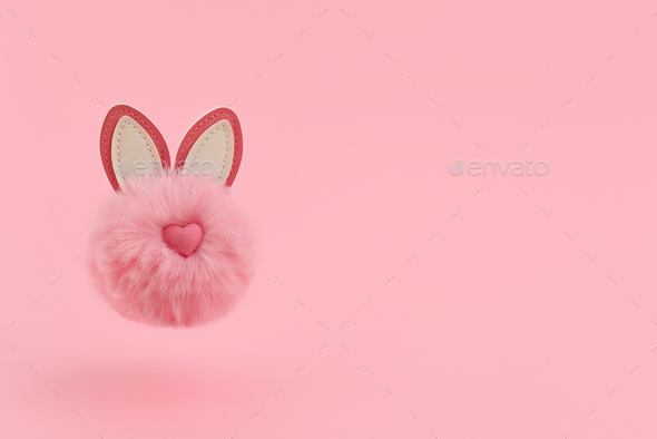 Creative flying fluffy rabbit pompon flies on a pink background.
