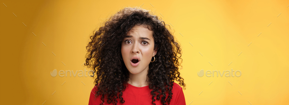 Confused and frustrated young questioned woman with curly hair open mouth and raising eyebrow in