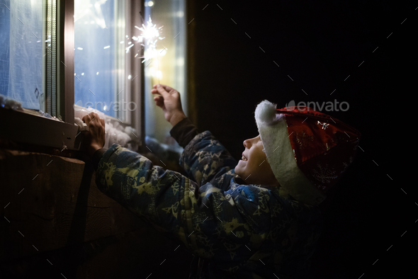 a child with sparklers looks out the window - Stock Photo - Images