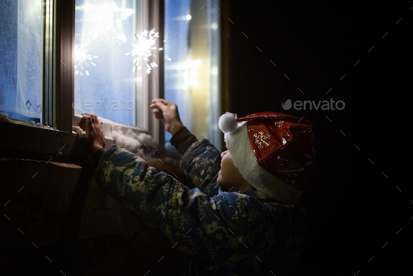 a child with sparklers looks out the window - Stock Photo - Images