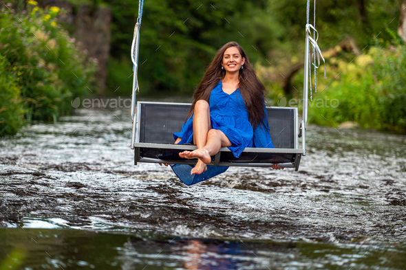 a joyful young woman swings on a rope swing across a fast-flowing