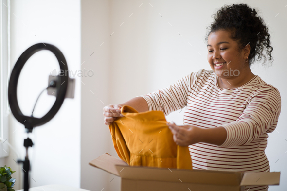 Emotional overweight woman fashion blogger showing brand clothes, unpacking parcel