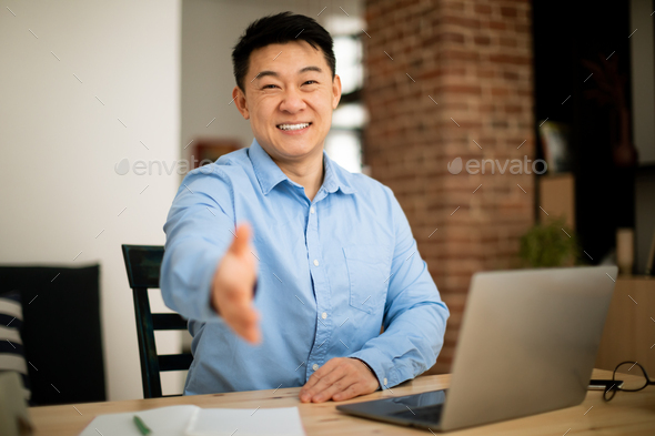 Employment concept. Asian mature entrepreneur stretching hand for handshake, sitting at workplace in