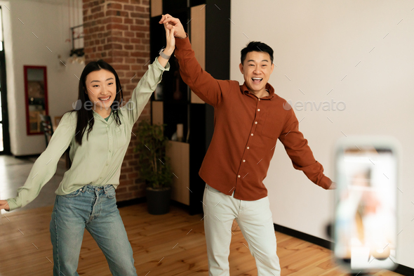 Couple of funny asian influencers shooting dance video for social network on cellphone, having fun