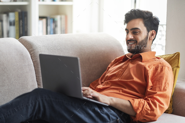 Middle eastern man chilling on couch at home, using laptop