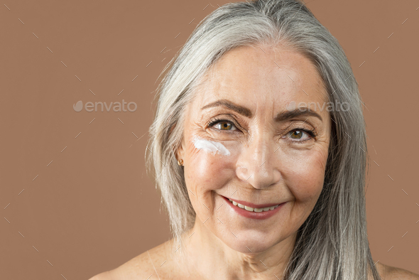 Happy old caucasian lady with natural beauty and cream on her face enjoy professional cosmetics