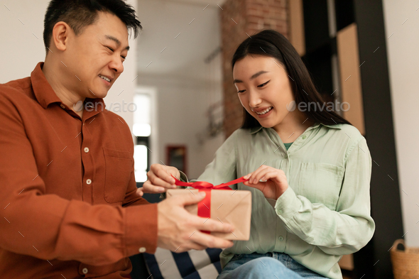 Romantic asian couple celebrating marriage anniversary or birthday, husband giving present to his