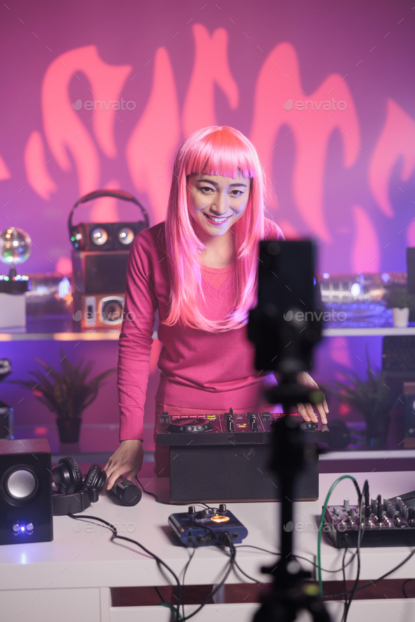 Dj with pink hair recording music session with smartphone camera while playing song at mixer console