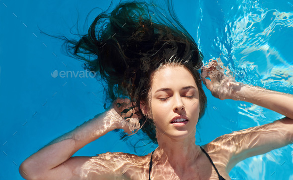 Summers here, time to go with the flow. Shot of a young woman in a swimming pool.