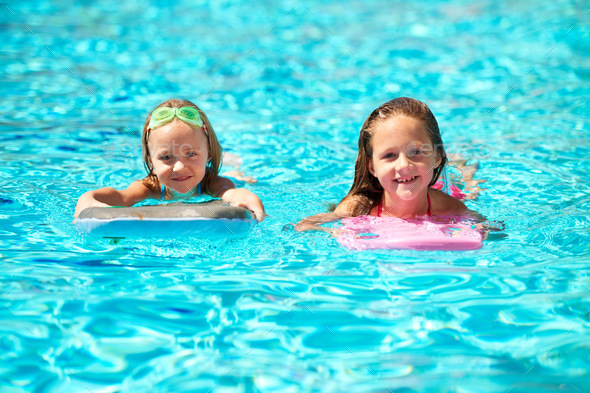 Summer rocks. Two little girls using pool inflatables while swimming ...