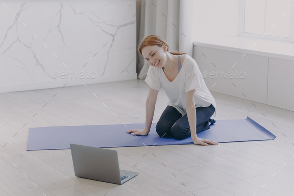 Happy caucasian woman has distance personal training in front of camera on yoga mat on floor.