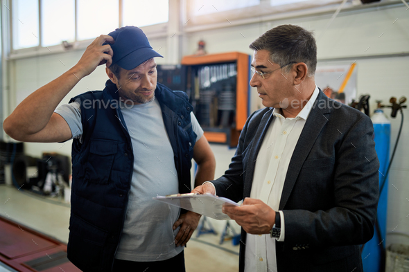 Businessman and auto mechanic going through paperwork in a workshop.