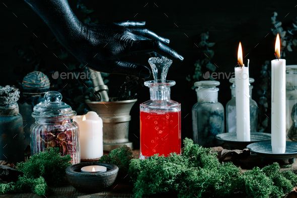 black witch hand opening magic potion, herbs ingredients candles and magical equipment