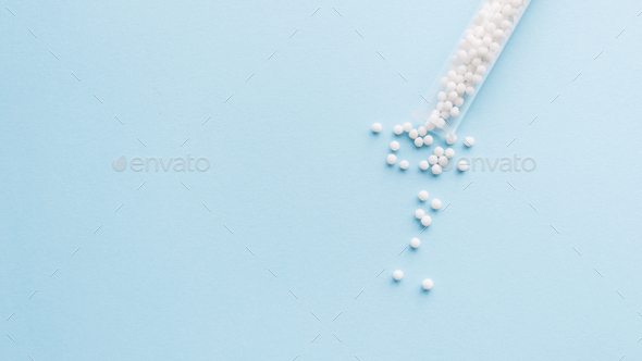 Homeopathic pills and a glass bottle on a light pastel background.