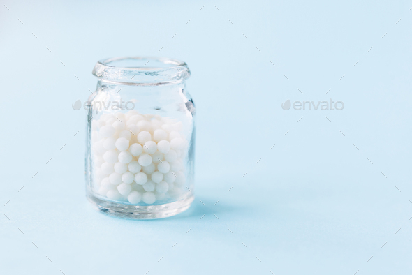 Homeopathic pills and a glass bottle on a light pastel background.