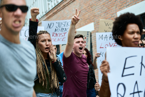 Young man with raised arms shouting while participating in anti-racism protest.