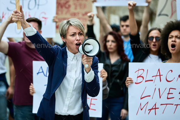 Caucasian woman leading anti-racism demonstrations and shouting through megaphone.