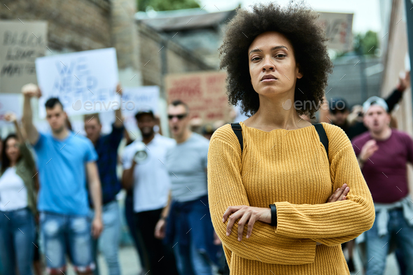 Young black woman standing with arms crossed while participating in anti-racism protest.