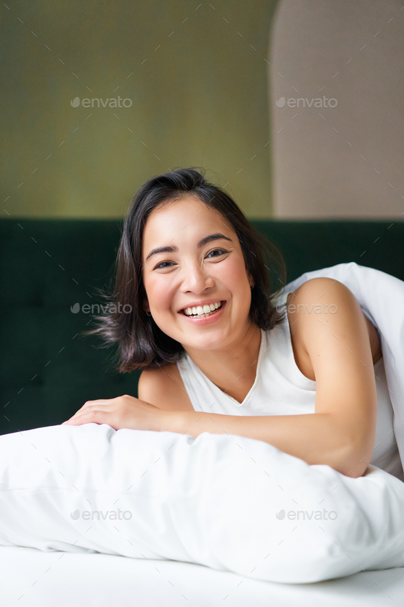 Vertical Shot Of Smiling Korean Woman Lying On Pillow In Her Bed Spending Morning In Bedroom 