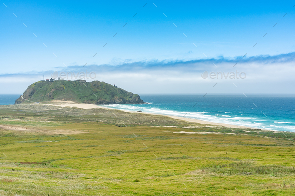 California, USA - May 19, 2018: grass covered land meeting the sea and a distant island in big sur