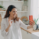 Young spanish woman has video call on phone at kitchen. Girl is waving hand and smiling. - PhotoDune Item for Sale