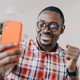 Happy african american man wearing glasses holding smartphone smiling reading good news message - PhotoDune Item for Sale