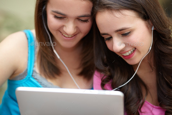 We share everything. Two teenage girls sharing earphones while looking a tablet.