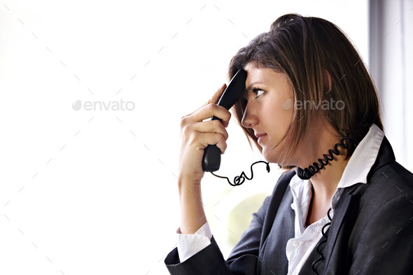 A bored businesswoman with a phone pressed to her head and the cord wrapped around her neck