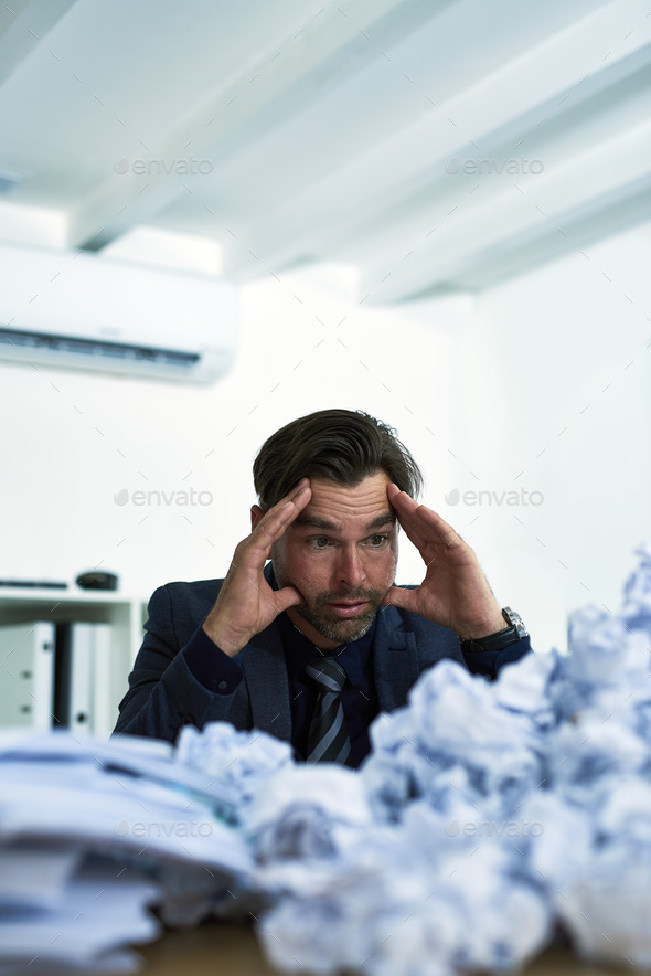 Shot of a stressed out businessman sitting at his desk overwhelmed by paperwork