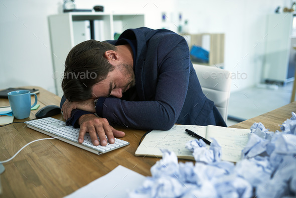 Shot of a stressed out businessman passed out at his desk overwhelmed by paperwork