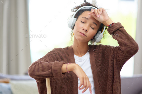 Shot of a woman wearing headphones and looking exhausted after cleaning her house