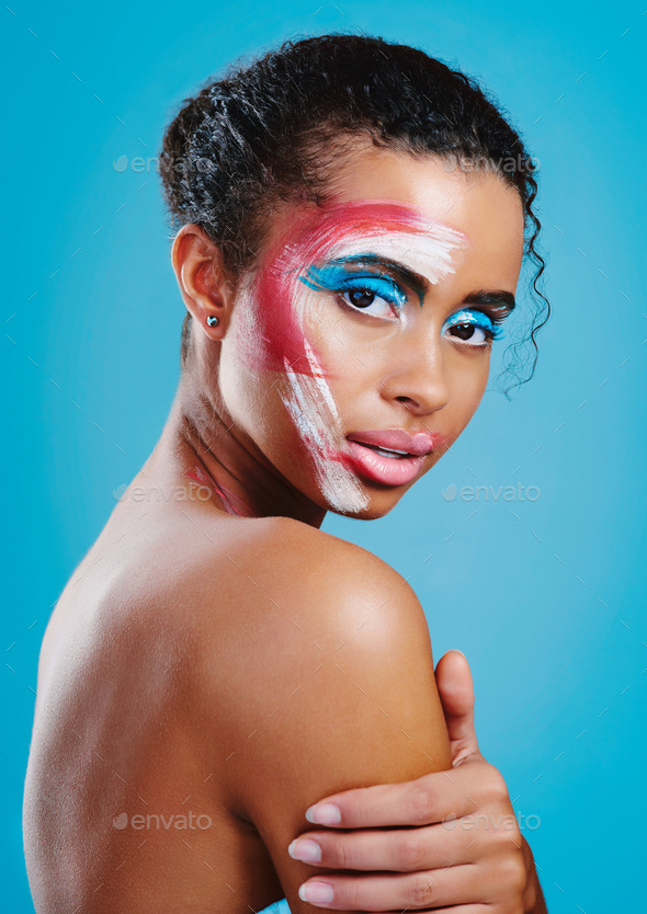 Studio portrait of a beautiful young woman covered in face paint posing  against a blue background Stock Photo by YuriArcursPeopleimages