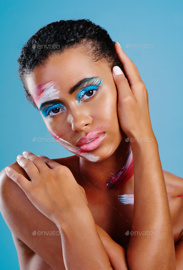 Studio portrait of a beautiful young woman covered in face paint posing  against a blue background Stock Photo by YuriArcursPeopleimages