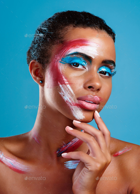 Studio portrait of a beautiful young woman covered in face paint posing  against a blue background Stock Photo by YuriArcursPeopleimages