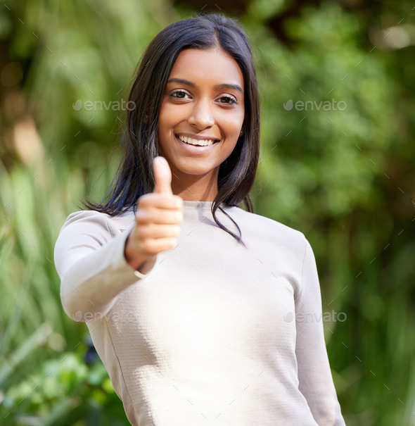 You got this. Shot of a beautiful young woman showing thumbs up while standing outside.