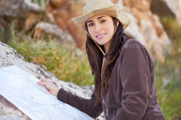 Navigating the hiking trail. A gorgeous young woman in a cowboy hat reading a map outside.
