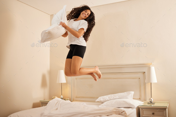 Can you tell how happy I am. Shot of a young woman jumping on her bed at home.
