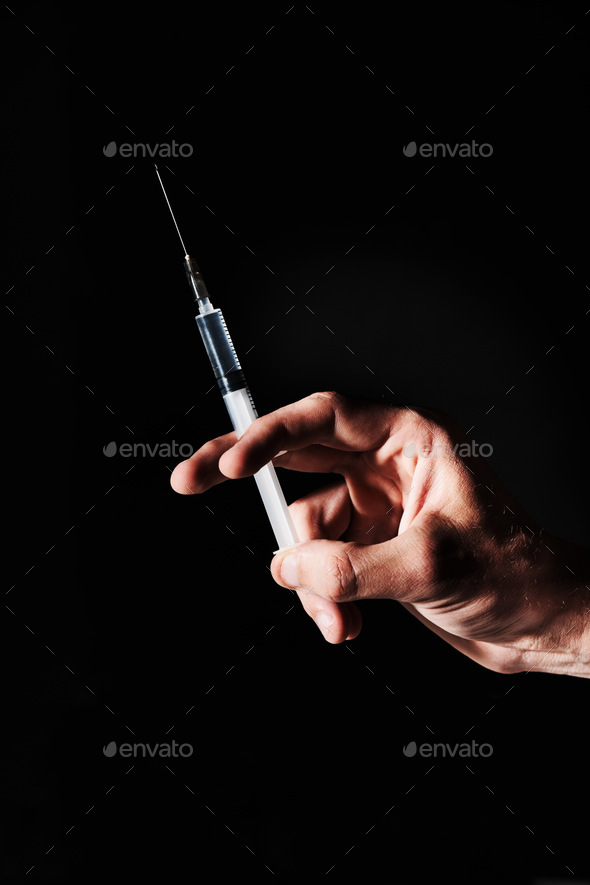 This wont hurt a bit. A hand holding a syringe against a black background.