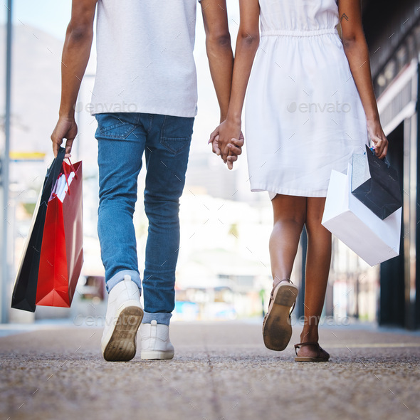 Shot of a young couple walking hand in hand while holding shopping bags