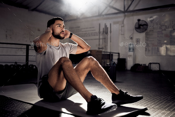 I lift heavy, work hard, aim to be the best. Shot of a young man doing crunches in a gym.