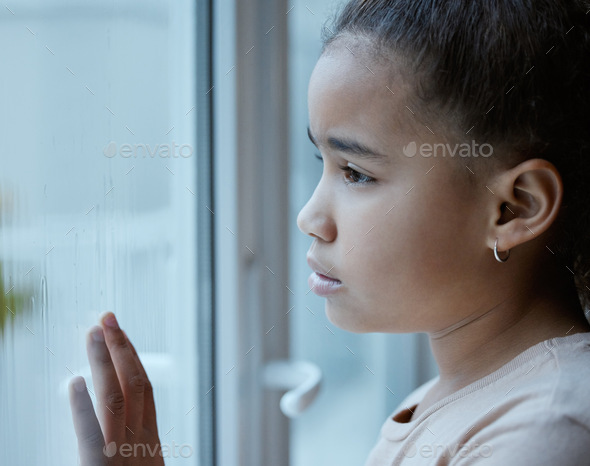 Shot of a little girl starting out of the window looking sad at home