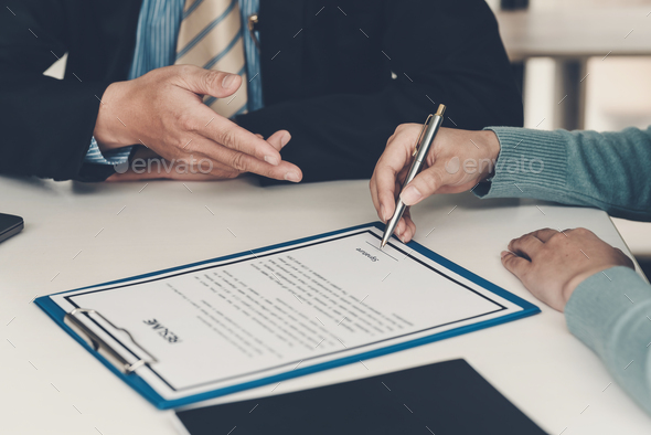 Close-up of a businessman hand pointing at a document to a client holding a pen to sign contract doc