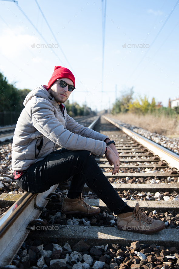 A man sits on the train track on a winter day, he is thoughtful and worried about the future