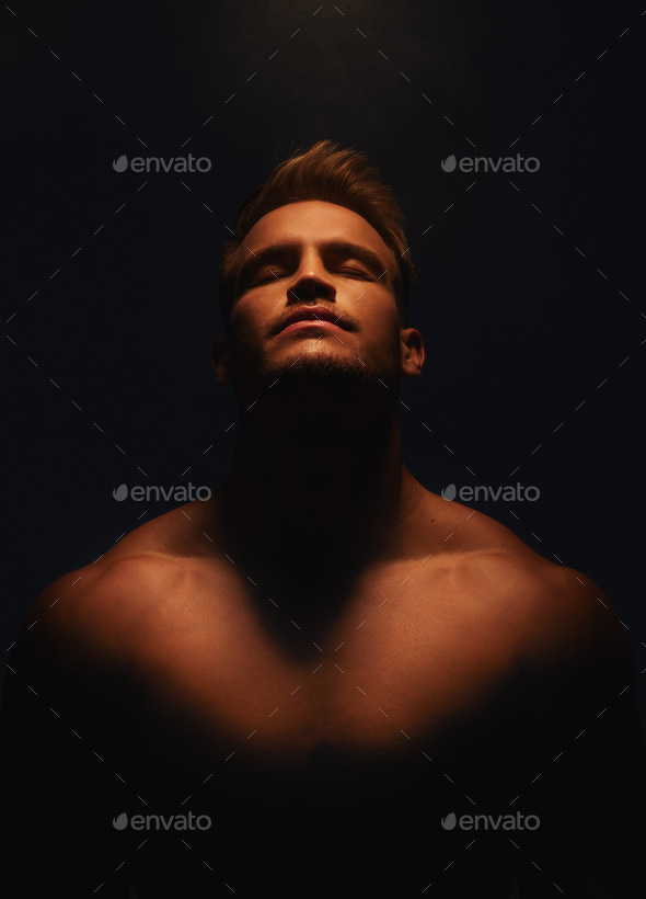 Shot of a handsome young man with no shirt on standing in the shadows