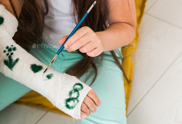 Girl drawing picture on bandage using paints close-up. Play therapy concept.