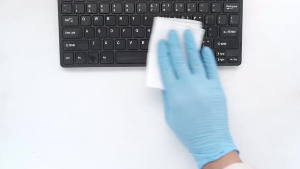 Hand in Blue Rubber Gloves and White Tissue Disinfecting Keyboard