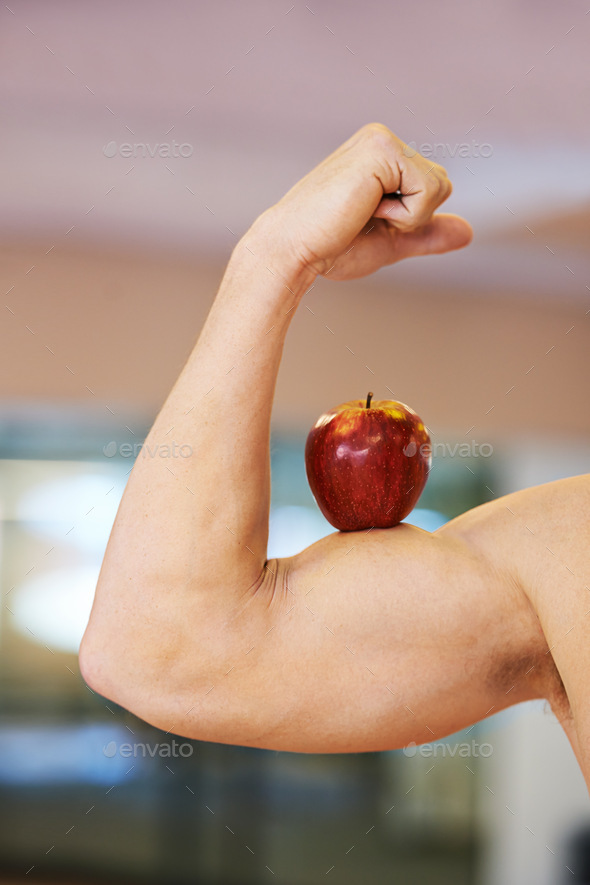 Perfect technique. Muscular man balancing an apple on his bicep.