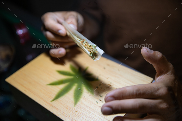 Close-up of the hands of a boy who is rolling a joint of marijuana. Focus on the marijuana
