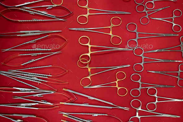 medical scissors and other basic stainless steel dental tools supplies on red fabric background