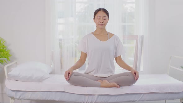 Calm of wellness Asian young woman sit on bed breathing with yoga lotus pose alt